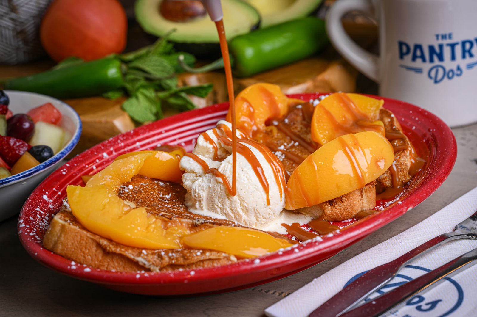 Peaches and cream French toast on a red plate with vanilla ice cream and caramel being poured over